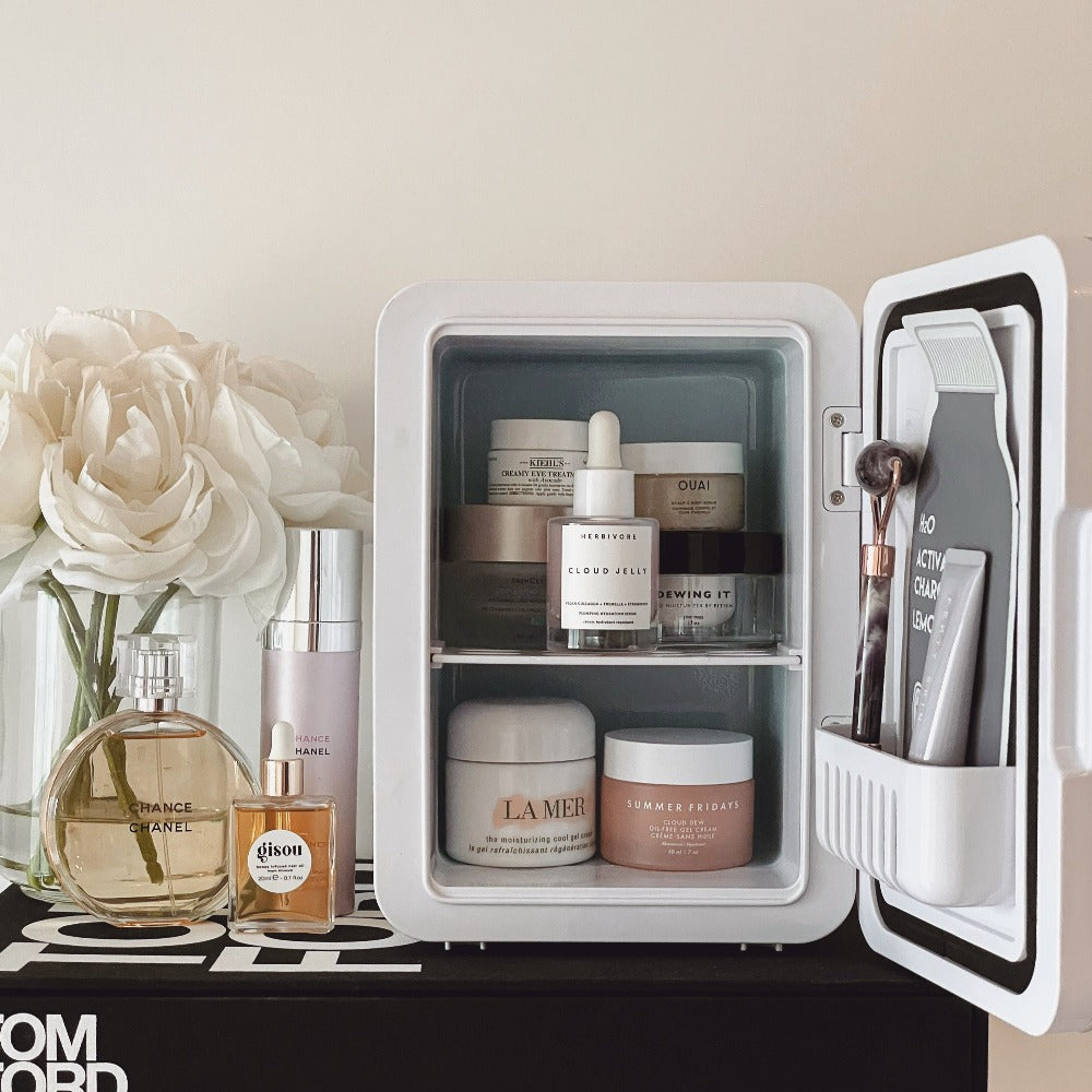 The White Marble Cosmetics Fridge on a vanity table filled with luxury skincare products and sheet mask. Nexy to flowers and makeup, cosmetics and perfume