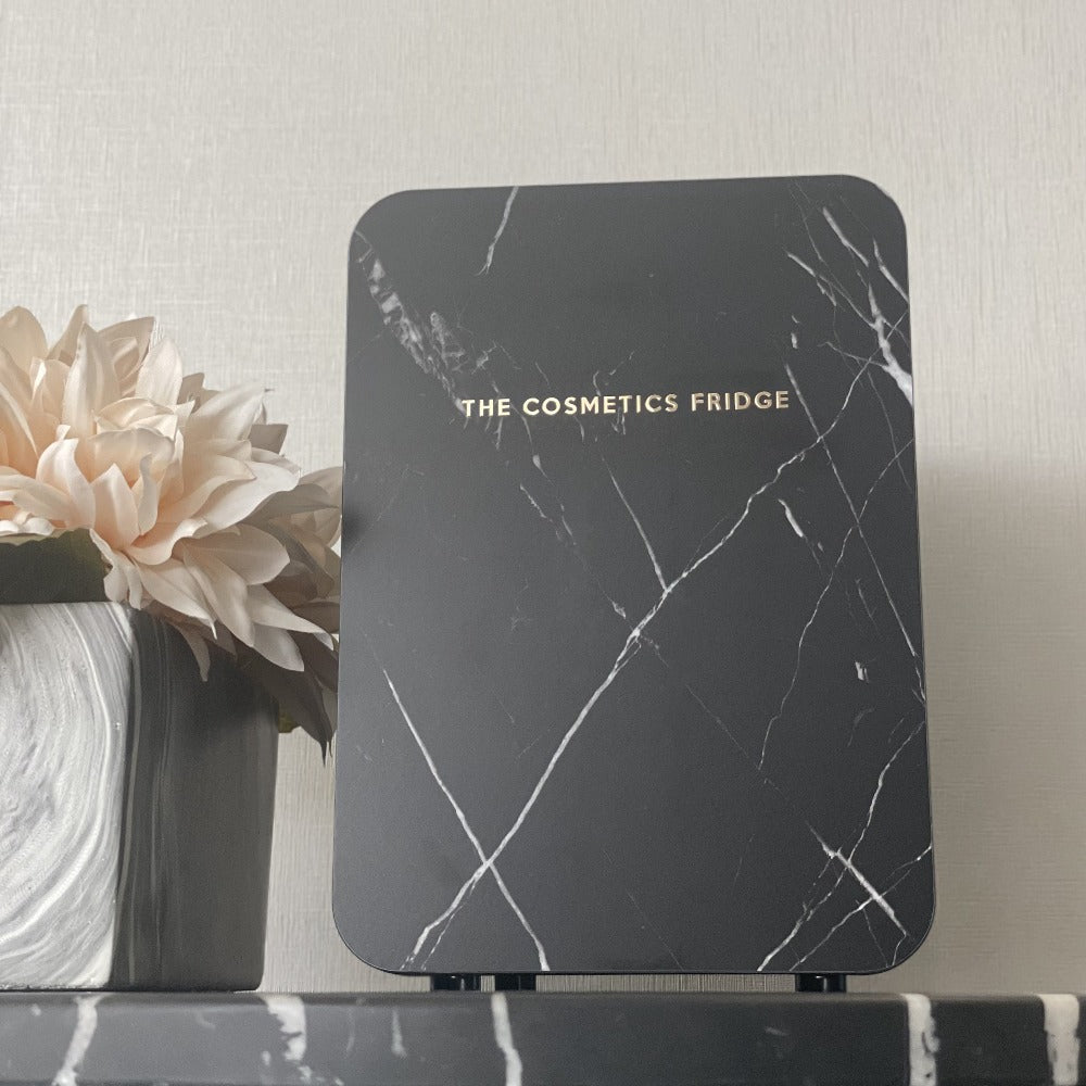 The Black Marble Cosmetics Fridge on a black marble table next to flowers